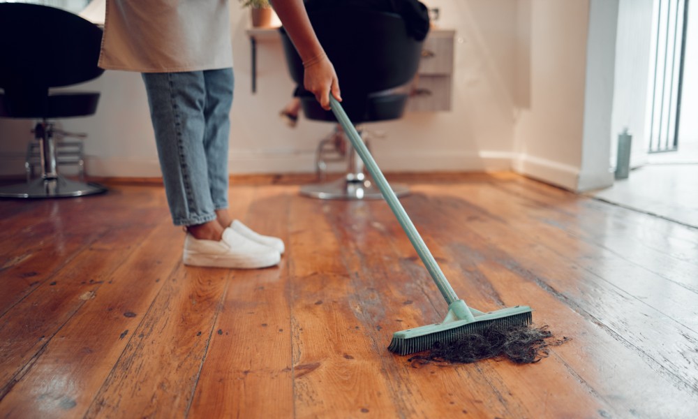 A woman sweeping hair off the wooden floor of a salon.