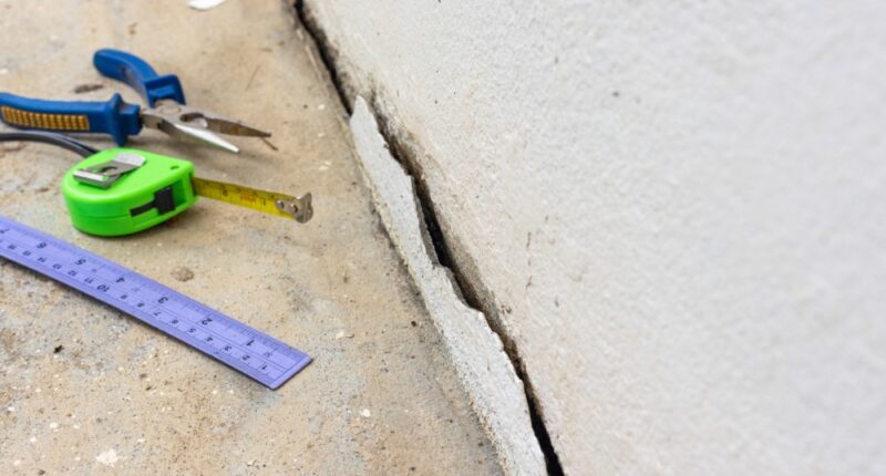 A crack in a home's concrete foundation with a ruler, a tape measurer, and pliers to the side.