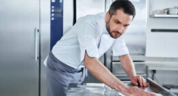 A professional chef cleans his commercial kitchen surfaces with a rag, ensuring a clean environment for food safety.