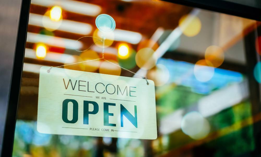 An 'Open' sign hanging on the entrance of a cafe or restaurant with the sun shining against the window.