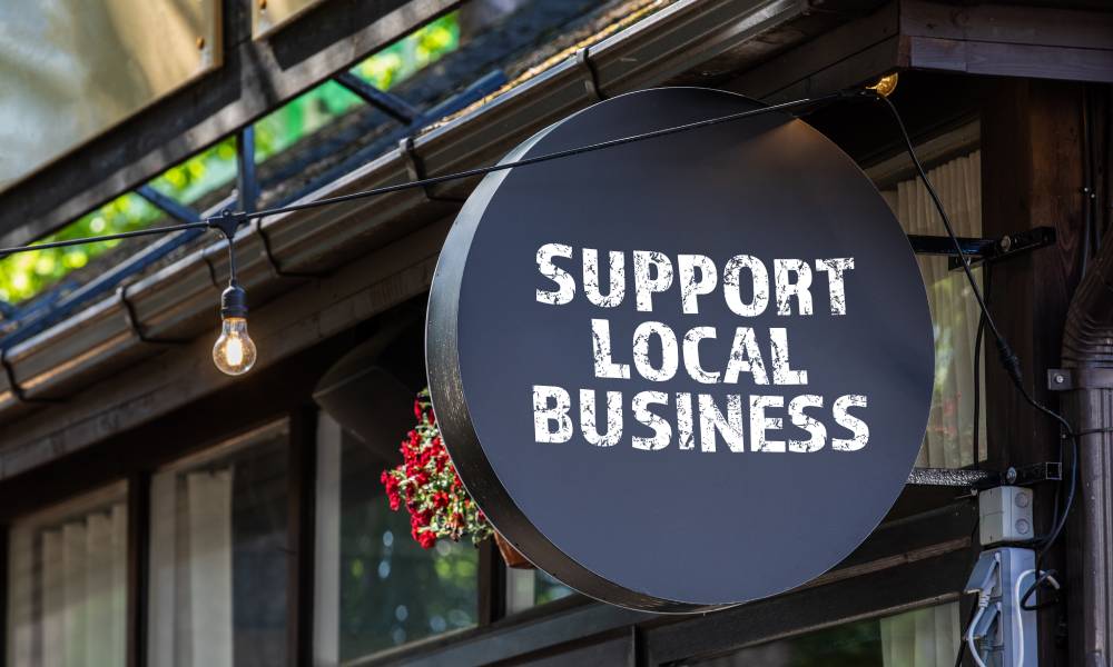 A round black sign hanging outside a small store says in white block letters "SUPPORT LOCAL BUSINESS."