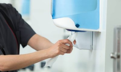 A man grabbing a paper towel from a wall-mounted, translucent, blue paper towel dispenser in a public restroom.