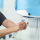 A man grabbing a paper towel from a wall-mounted, translucent, blue paper towel dispenser in a public restroom.