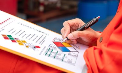 A safety engineer using a pen to make a mark on a health risk assessment sheet on a page with chemical symbols.