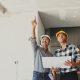 A homeowner stands in his home with a contractor while looking at blueprints. The house is undergoing renovations.