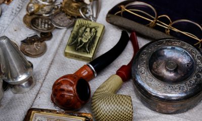 A close-up of a table with antique items, including smoking pipes, reading glasses, coins, and a lighter.