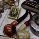 A close-up of a table with antique items, including smoking pipes, reading glasses, coins, and a lighter.