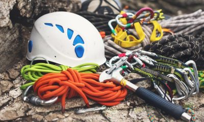 Different hiking gear rests on a rock. A white hard hat, various ropes, and carabiners are laid out.