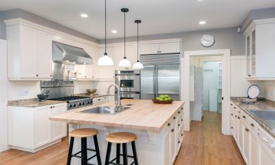 A luxurious kitchen contains white cabinets, a large island, a stainless steel refrigerator, and two sinks.