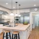 A luxurious kitchen contains white cabinets, a large island, a stainless steel refrigerator, and two sinks.
