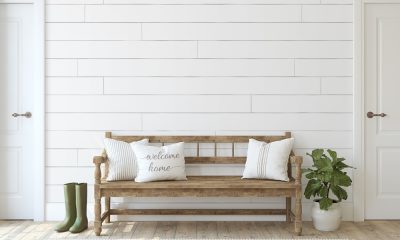 A wooden bench sits in a hallway with three throw pillows. One pillow contains the phrase "Welcome Home."