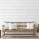 A wooden bench sits in a hallway with three throw pillows. One pillow contains the phrase "Welcome Home."