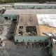 A aerial view of a large, green commercial building with the roof torn off in the aftermath of a tornado.