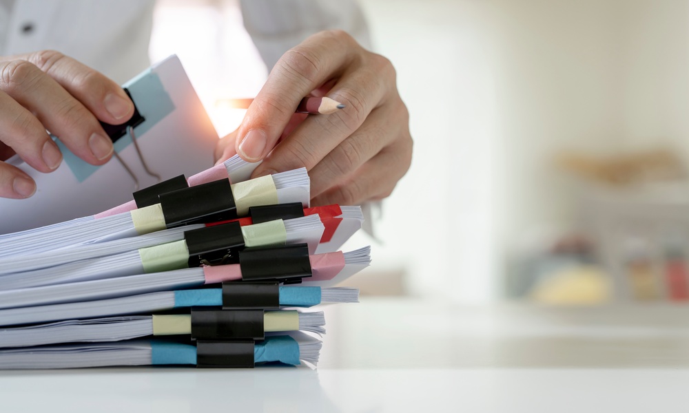 A person sorts through a stack of sorted paperwork, each mini stack has a black binder clip holding them together.